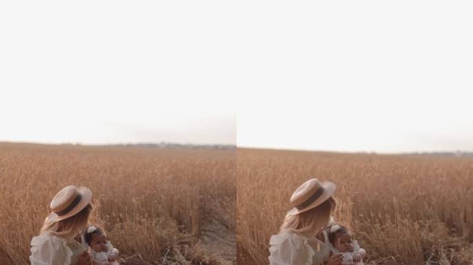 年轻美丽的母亲坐在草地上，在夕阳下抱着她的孩子，拥抱和亲吻她的女儿。母亲对孩子的爱。阖家欢乐，母亲节