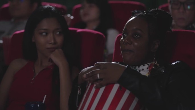 两个年轻女子喜欢在电影院看电影。女性朋友在电影院看电影时分享爆米花。两个年轻的女性朋友在电影院看电影