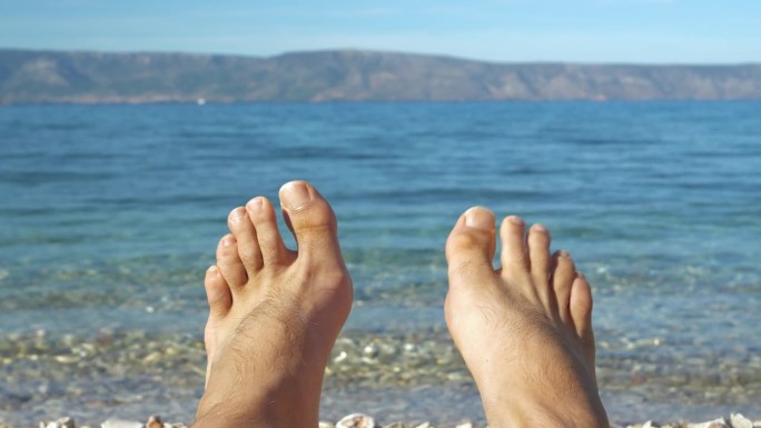 特写，DOF:在蔚蓝的海边，阳光明媚的亚得里亚海海滩上，光着脚扭动的男性