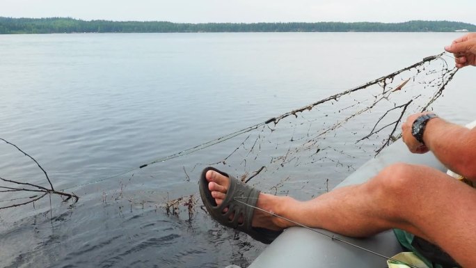 休闲钓鱼，网偷猎。在卡累利阿的Losossinnoye湖，一名渔民坐在一艘橡皮艇上，用树枝拉出一张破
