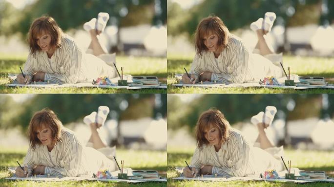 一位女画家躺在草地上，微笑着在速写本上画画
