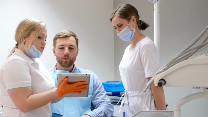 一位英俊的年轻病人在两位女牙医的陪伴下看着苹果智能手机