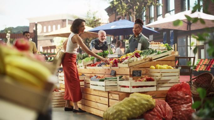 西班牙女顾客向一对多民族农民夫妇购买两个蒜头和一个菠萝。成功的成年人在城市广场市场管理小型商业农场摊