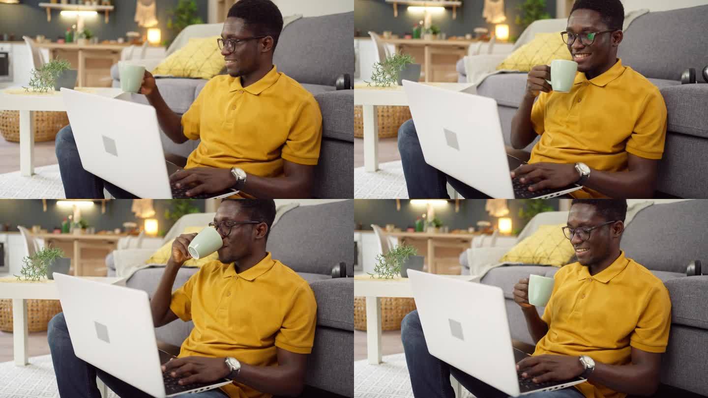 一名非裔美国人一边在家用笔记本电脑工作，一边喝咖啡