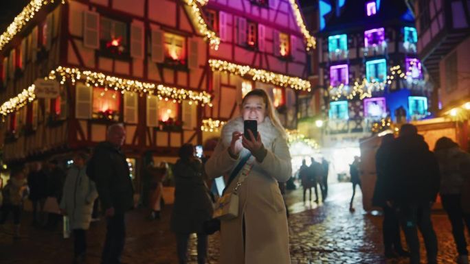 在科尔马镇一个热闹的圣诞市场上，一名女子边逛边用她的智能手机