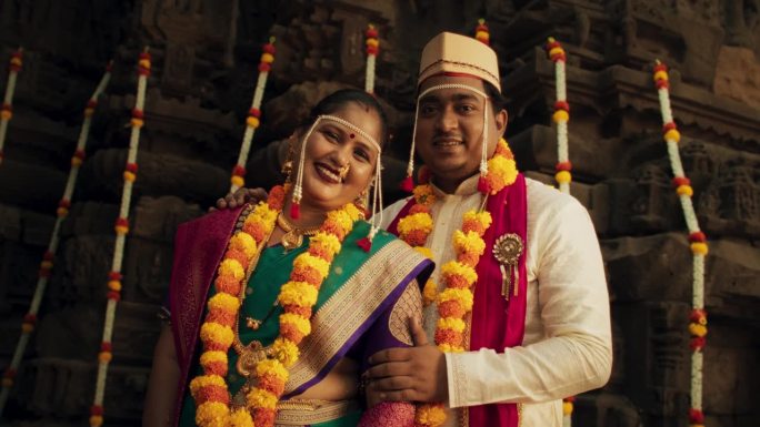 幸福的印度夫妇看着相机，在他们的传统婚礼上拍照。新娘和新郎穿着漂亮的彩色衣服庆祝他们的爱情和结合的真