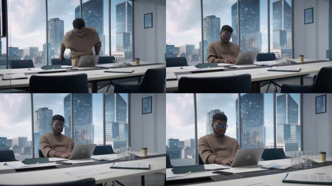 自信的商人坐在现代办公室的办公桌前，使用笔记本电脑，旁边的窗户可以看到大城市的摩天大楼。成功的财务经