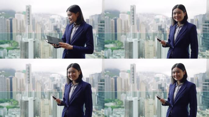 年轻的女商人独自站在外面，用着平板电脑，背景是香港岛的建筑。