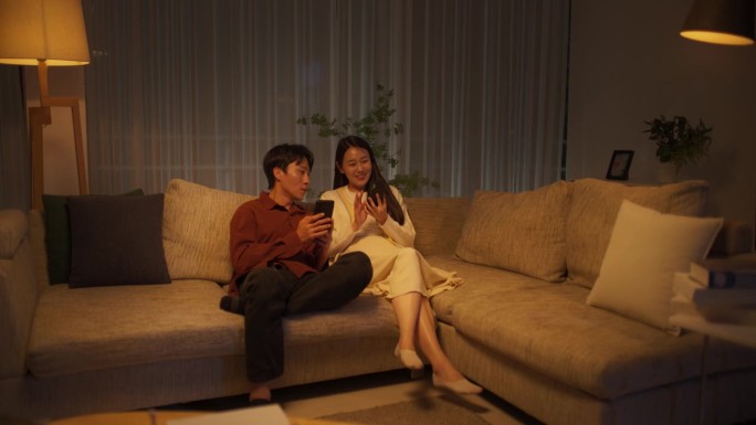 韩国夫妇晚上在家享受休闲时光，两人都用智能手机网购。寻找特价商品的男人和女人。女友向男友寻求建议