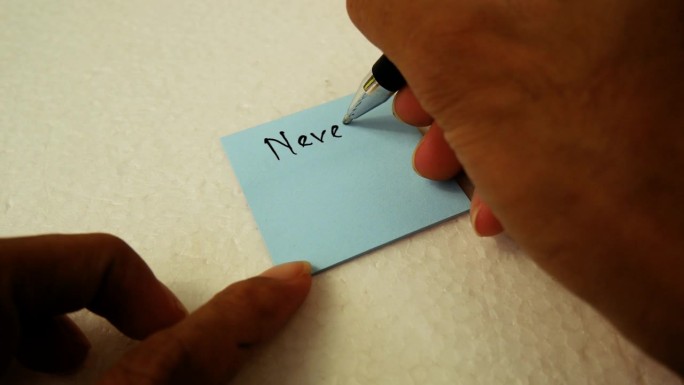 一个男人的手在粉红色的便条纸上写着“永不言弃”