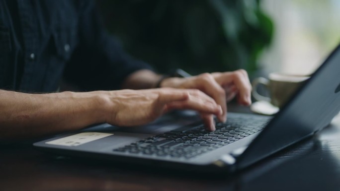男性IT专业人员的手在笔记本电脑的键盘上，特写，从咖啡馆远程工作的人