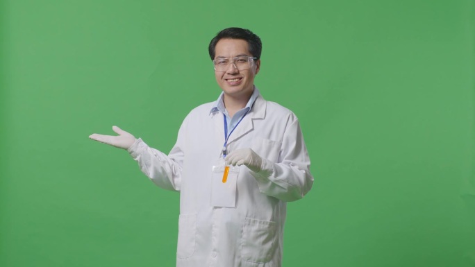 亚洲男性科学家，试管里有橙色液体，站在实验室的绿色背景屏幕上微笑着指着一边
