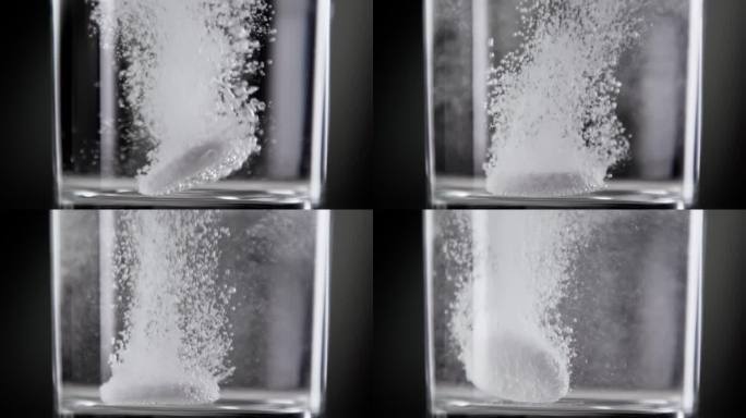 泡腾片落入玻璃杯中的淡水(特写)。在演播室拍摄的宏观上制作运动生活方式的健康饮料。服用止疼药丸和悬浮