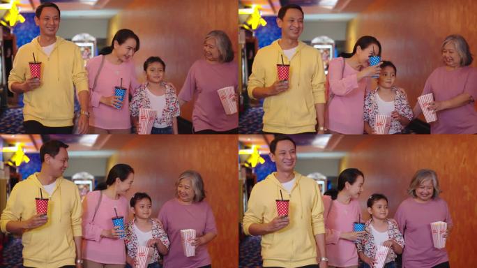 快乐的亚洲家庭带着爆米花和饮料准备一起去电影院看电影。亚洲家庭拿着碳酸饮料和一桶爆米花去电影院看电影