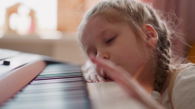 昏昏欲睡的小女孩躺在家里敲击钢琴键
