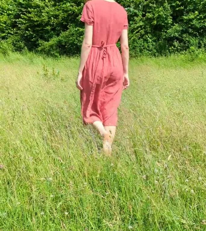 美丽的白种女人，穿着红衣服，微笑着走在夏日的田野上。呼吸新鲜空气，和谐放松。人与自然的统一。垂直的画