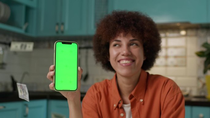 女性手中的绿屏手机上的美元。黑人女性展示彩色键智能手机，现金在慢镜头中掉落。