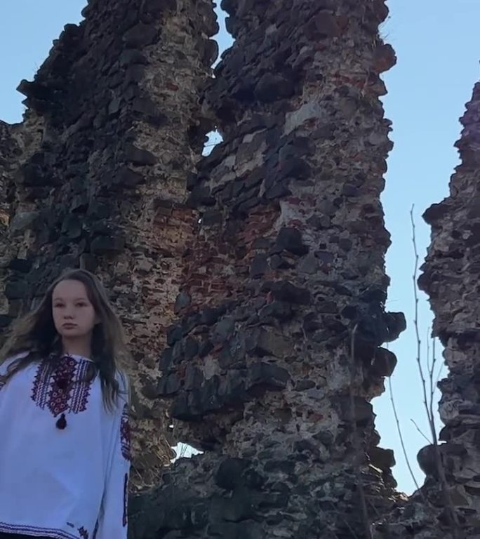没有战争的乌克兰年轻女孩在一个古老的城堡废墟上，穿着刺绣衬衫，悲伤地看着周围的一切