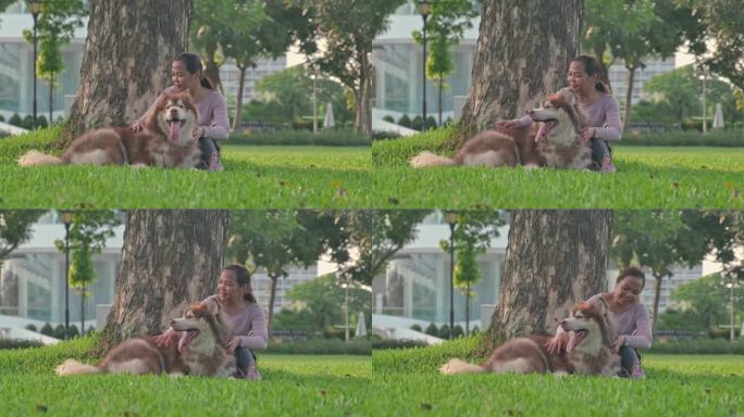 在大公园的草地上，一位亚洲妇女和她的狗坐在一起