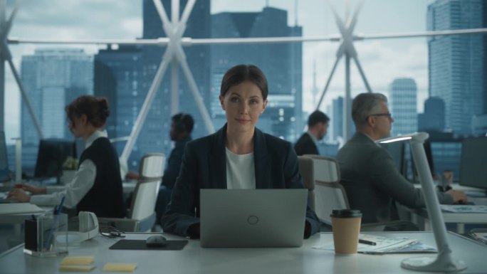 裁员、裁员和压力概念:市中心摩天大楼办公室里用笔记本电脑工作的女性项目经理。女商人看着镜头。戏剧性蓝