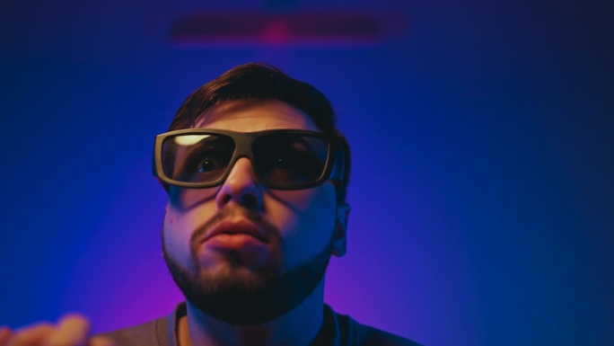 一个男人在黑暗的房间里享受电影之夜，有霓虹灯，爆米花，戴着3D眼镜