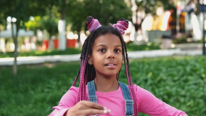 一个梳着粉色辫子的非裔美国女孩在城市街道上像个洋娃娃。