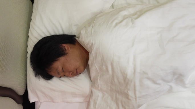 从自上而下的角度来看，一个疲惫的男人整夜在床上翻来覆去，与不安的睡眠和失眠的挑战作斗争。这种健康问题