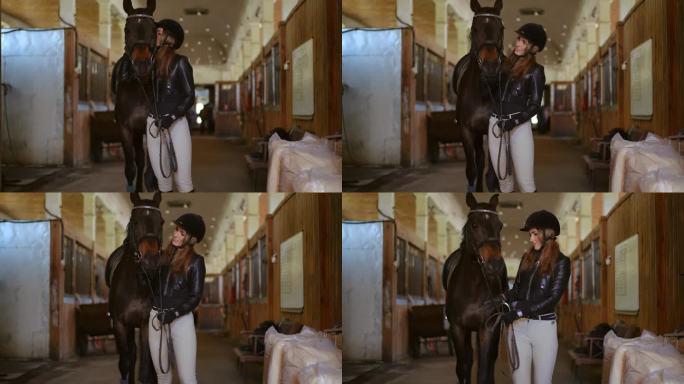 年轻的女人微笑着亲吻拉着缰绳的马，开始在谷仓里走。肖像自信积极的高加索女马术与优雅的纯种动物在马厩室