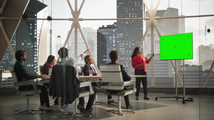 多样化的印度办公室会议室:年轻的女经理为企业家做演讲，用绿色屏幕模拟显示的电视。商人谈论金融市场