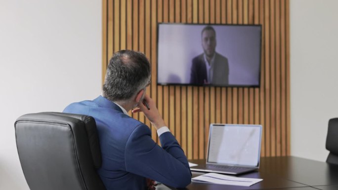 商人在电视机上与同事视频通话的后视图