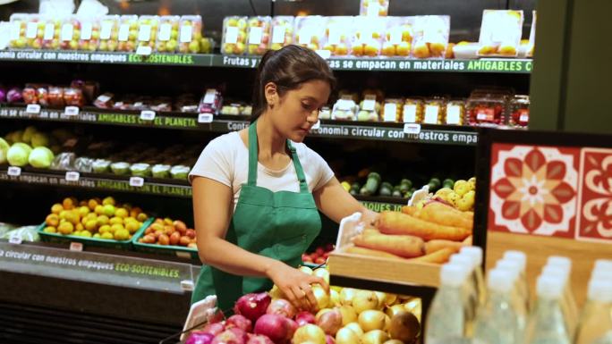 拉丁美洲的女售货员在超市检查洋葱的陈列