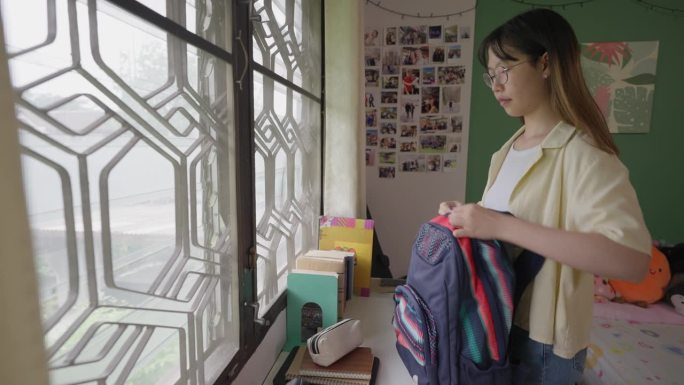 年轻的女学生在她的房间里，上学前把学习材料放进书包里