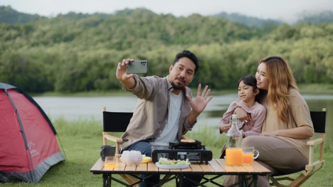 幸福的一家人在湖边的露营地用照相手机自拍。