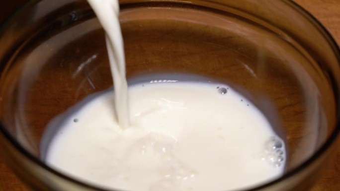 鲜牛奶倒进木桌上的碗里。