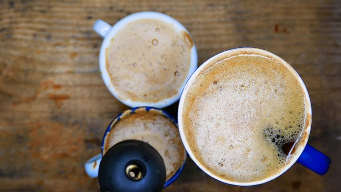 漂亮的奶油咖啡杯:一个人用水壶把开水倒在三杯奶油咖啡上。桌上有一杯咖啡。表格，俯视图。热气从热咖啡中