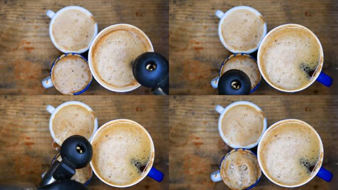 漂亮的奶油咖啡杯:一个人用水壶把开水倒在三杯奶油咖啡上。桌上有一杯咖啡。表格，俯视图。热气从热咖啡中