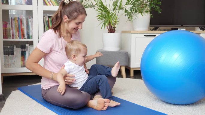 一位年轻的母亲带着她的小儿子在客厅的垫子上健身时玩着健身球。医疗保健、体育、儿童保育和儿童发展的概念
