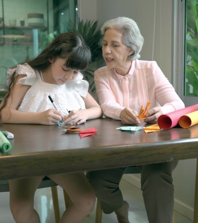 一个家庭花时间一起在家制作工艺品。快乐的奶奶和孙女在周末用折纸制作红色和橙色的卡通。休闲活动。孩子们