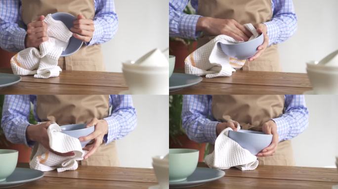 女性用白色的华夫饼织毛巾擦盘子。在一个质朴的厨房里，穿着米色围裙的女人在擦拭洗过的盘子