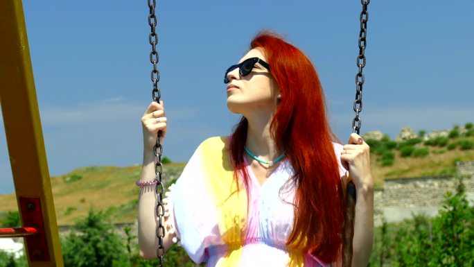 红头发的年轻女子在公园里荡秋千