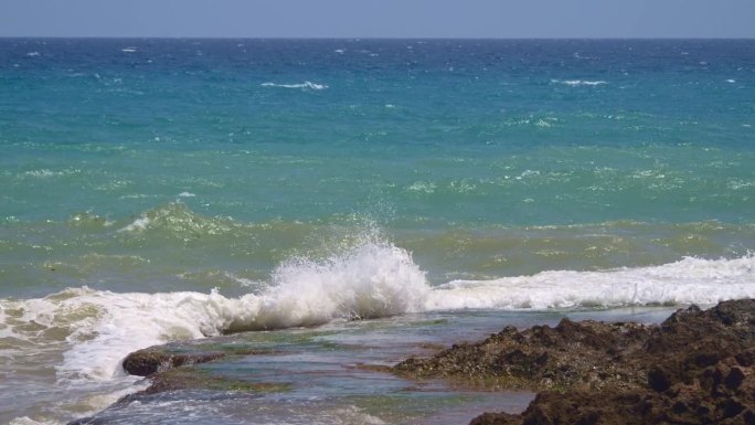 阳光照耀在汹涌的水面上，海浪拍打着海岸，溅起水花和泡沫。