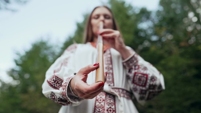 手的妇女演奏木管木笛-乌克兰特伦卡或泰林卡在森林背景。民间音乐概念。乐器。身穿传统刺绣衬衫的音乐家。