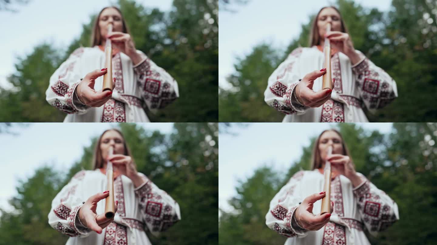 手的妇女演奏木管木笛-乌克兰特伦卡或泰林卡在森林背景。民间音乐概念。乐器。身穿传统刺绣衬衫的音乐家。