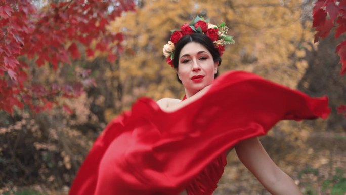 一位身穿红裙、头戴花圈的女士在表演秋舞。秋天公园里的女孩。