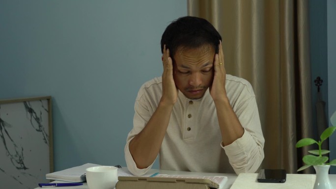 在家工作的亚洲男性因工作时间过长而头痛。办公室综合症。