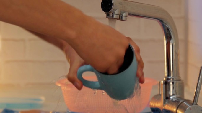 在厨房里，男人一边用清洁垫、肥皂和水擦盘子，一边用双手。