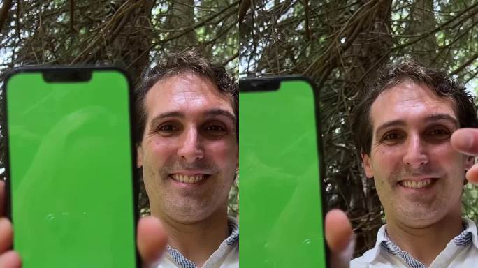一个男人手里拿着绿屏色度键的手机，他穿着白衬衫站在森林里向镜头展示手机