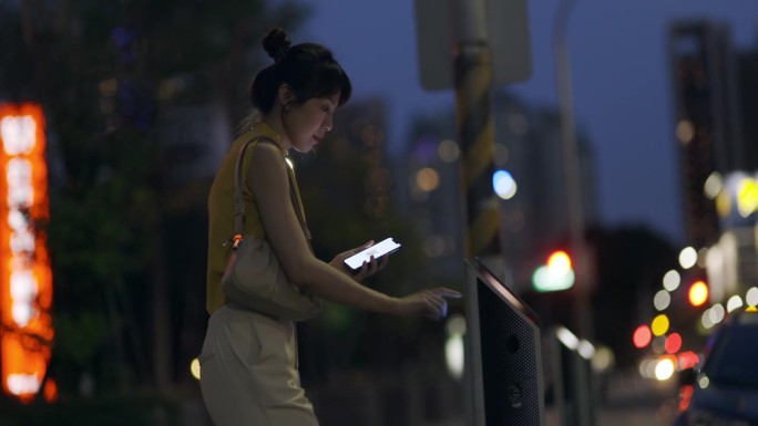 夜间，一名亚洲女性在城市里用手机支付停车费，她接受了数字钱包和多种支付方式的概念。