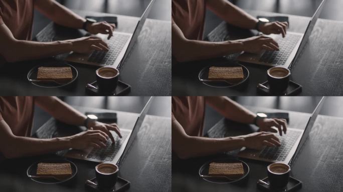 在咖啡馆用笔记本电脑工作的男子，近距离观察在键盘上打字的年轻男子的手