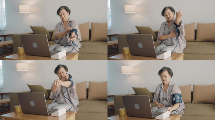 亚洲老年人呆在家里，使用电脑，并尝试使用数字血压计来检查她的血压和脉搏。